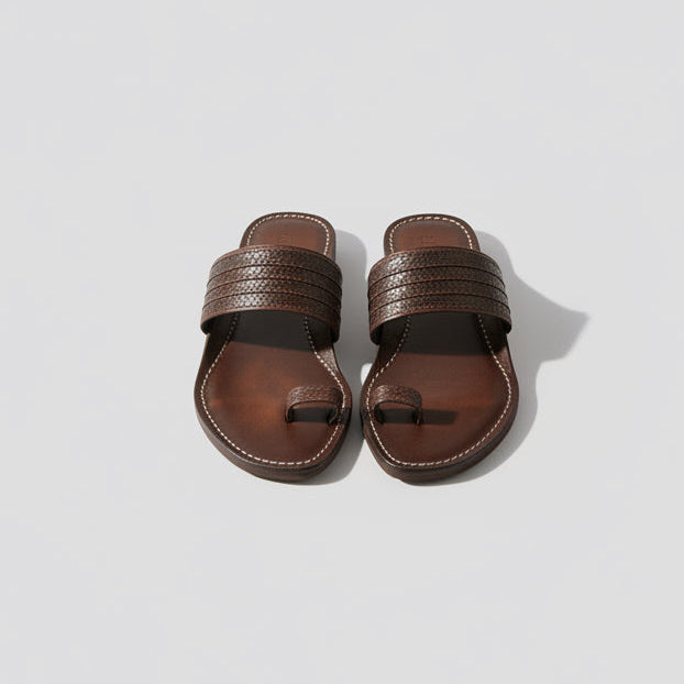 Brown sandals on a light wooden floor with three ceramic vases against a white wall.