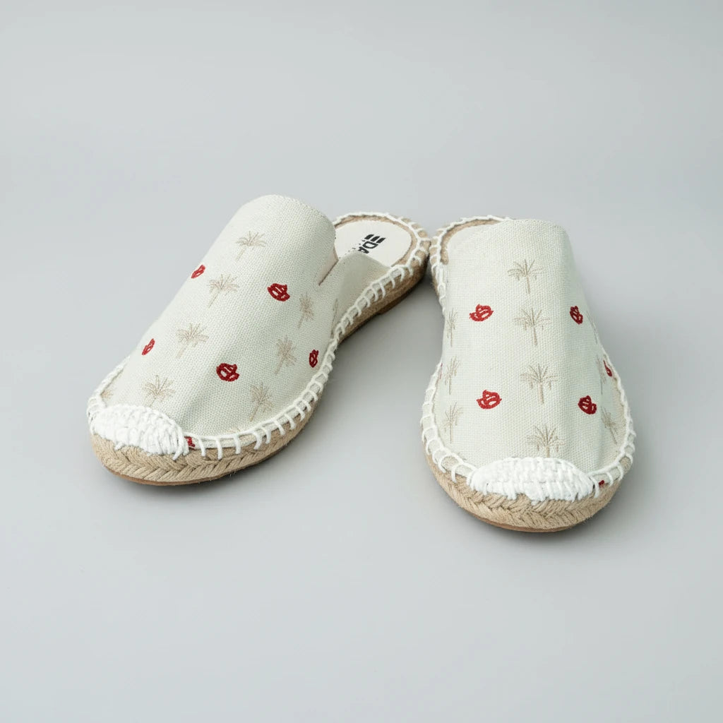 Pair of white slippers with red floral patterns on a white background