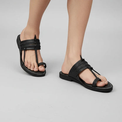 A pair of black leather thong sandals with braided straps and contrast white stitching, shown on a model's feet against a light gray studio background.