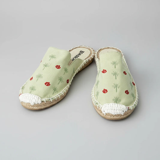 Pair of light green espadrille shoes with red floral patterns on a white background