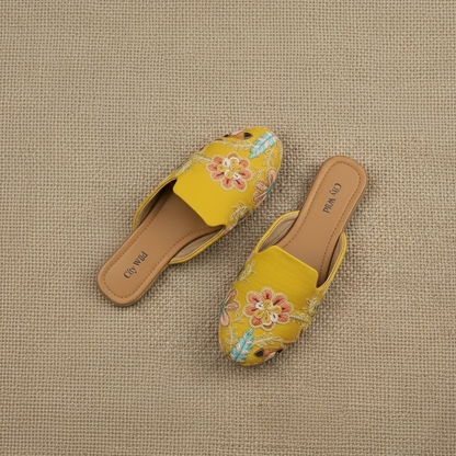 Yellow saree with floral patterns, matching shoes, and jewelry on a textured surface with flowers.