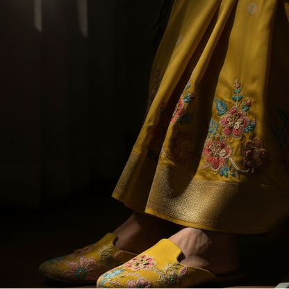 Person wearing a yellow traditional outfit with floral patterns sitting on a chair.