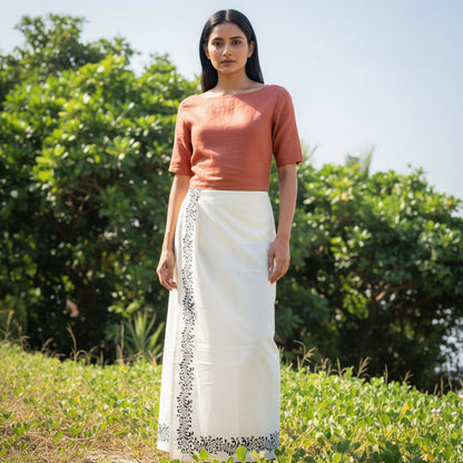 Person wearing a white dhoti with black embroidery standing in a field.