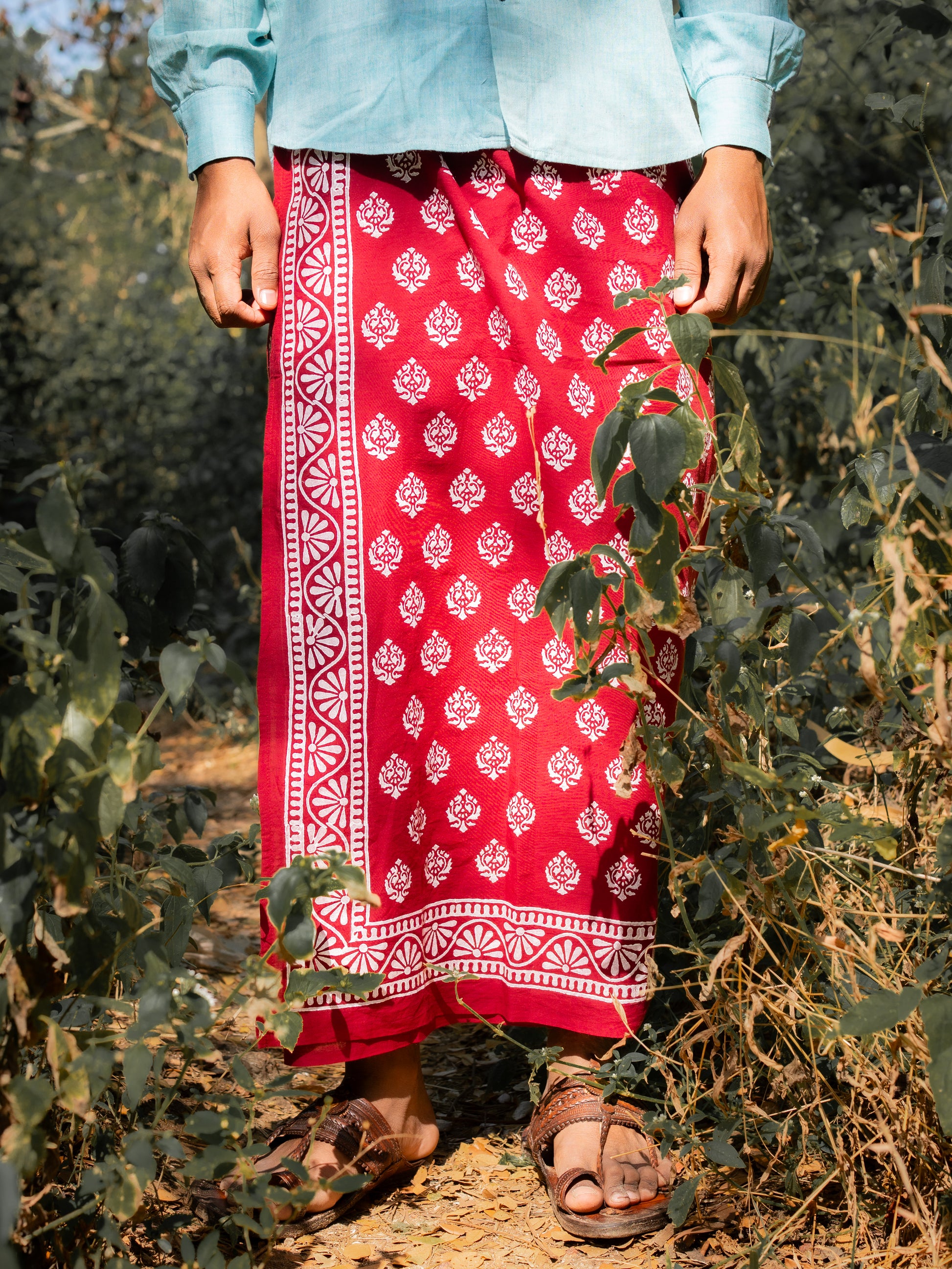 Person wearing a red patterned skirt and light blue top standing in a natural setting.