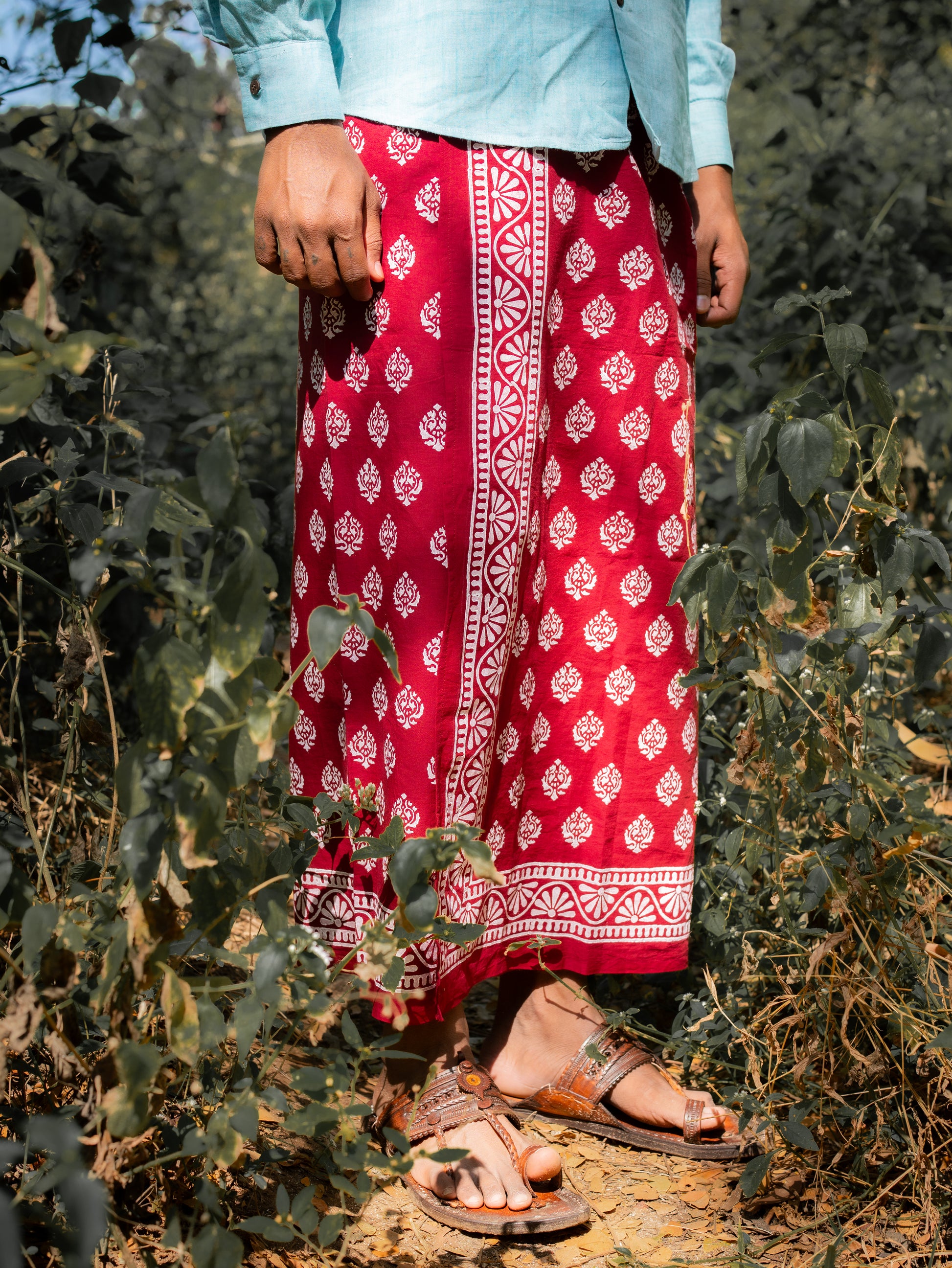 Person wearing a red patterned skirt standing among green plants