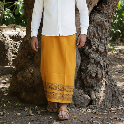 Person wearing a white shirt and yellow skirt with a patterned hem, standing against a stone wall.
