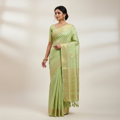 Green woven mat with tassels on a textured surface with leaves and decorative items.