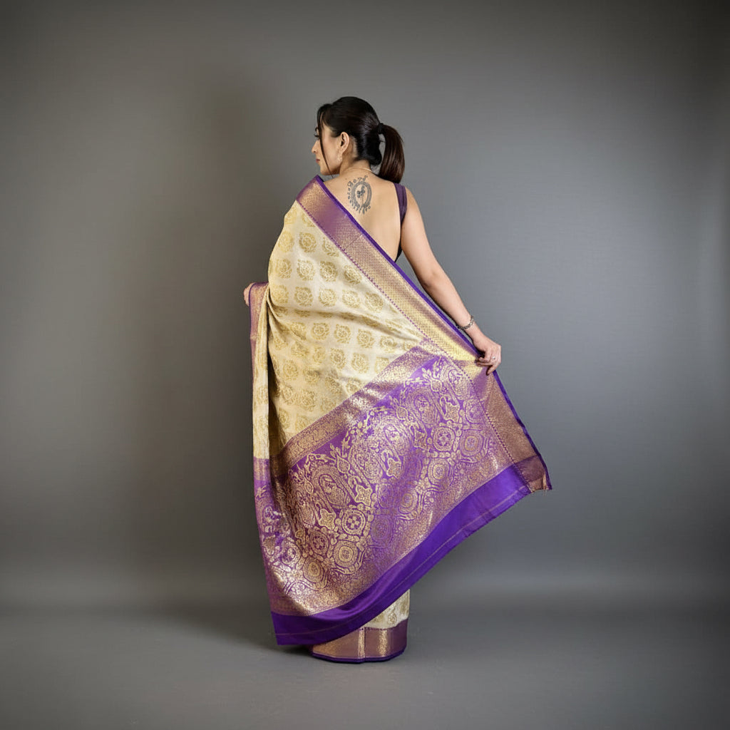 Woman holding a purple and gold saree in a room with a plant and chair.