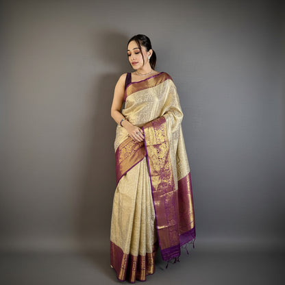 Woman wearing a traditional saree with a gold and purple design against a plain background