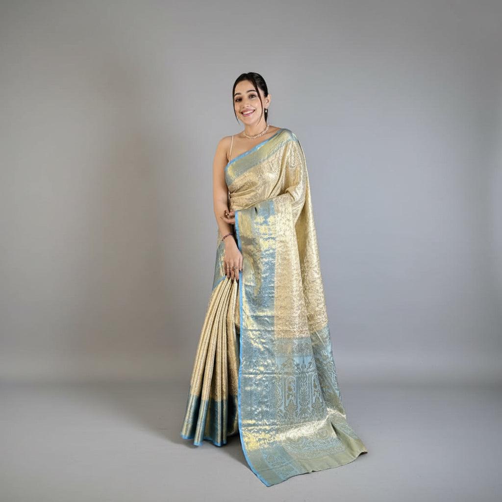 Woman in a gold and blue saree standing in a room with a plant and chair.