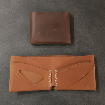 Two brown leather wallets on a light wooden surface
