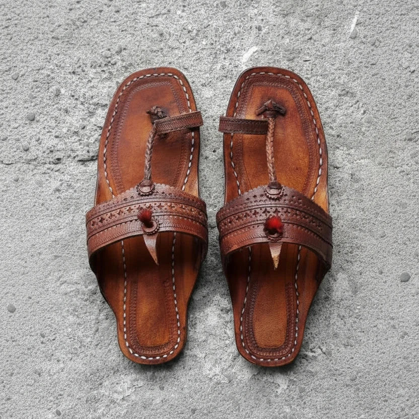 Pair of brown leather sandals with decorative straps on a gray surface