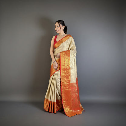 Woman in a traditional saree standing against a gray wall with a plant and chair in the background.