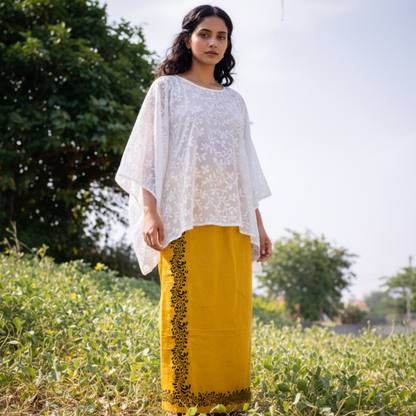 Woman wearing a white top and yellow skirt with black patterns in an outdoor setting