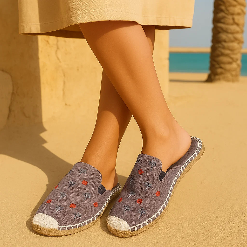 Person wearing gray espadrilles with floral patterns on a sandy background