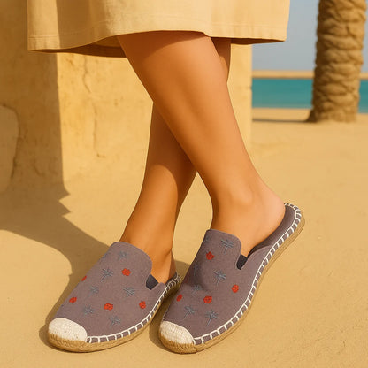 Person wearing gray espadrilles with floral patterns on a sandy background