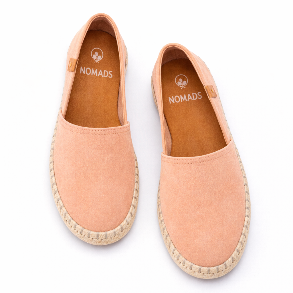 Pair of peach-colored espadrilles with 'Nomads' branding on a white background