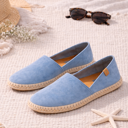 Pair of light blue espadrilles on a textured surface with a hat, sunglasses, and starfish.