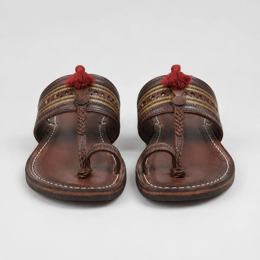 A pair of brown leather thong sandals with decorative woven straps, white stitching, and red tassels on a light gray background.