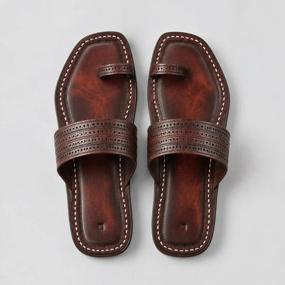 A pair of dark brown leather flat sandals with decorative perforated straps and contrast stitching, shown from a top-down view on a light gray background.