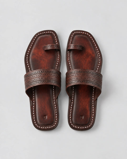 A pair of dark brown leather flat sandals with decorative perforated straps and contrast stitching, shown from a top-down view on a light gray background.