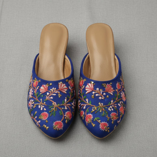 Pair of blue embroidered slippers with floral patterns on a white background