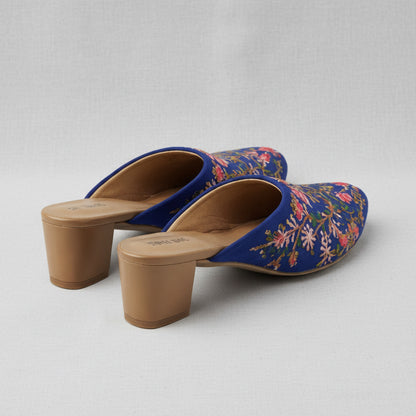 Blue floral embroidered mules with tan soles on a white background