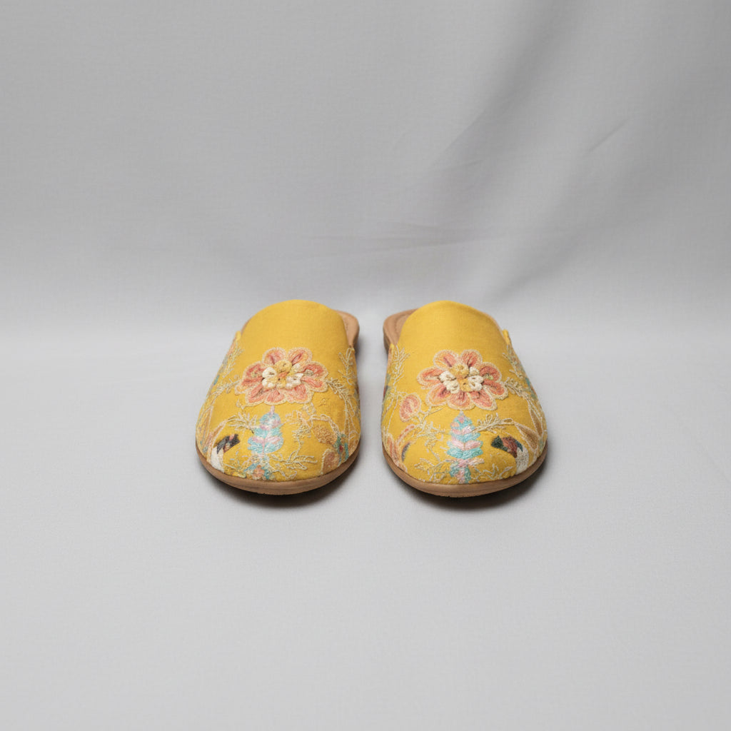 Pair of yellow slippers with floral embroidery on a white background